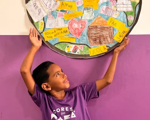 Aluno com mãos levantadas sobre a cabeça com um mapa do mundo com frases de amor e paz feito pelos coloridos